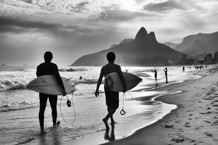 people on beach going surfing black and white
